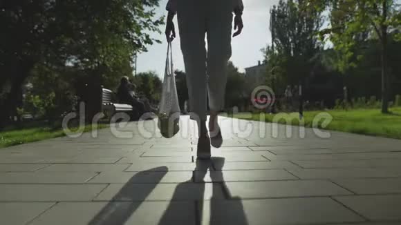 妇女的正面景色手里拿着带水果的棉网购物袋在夏季公园散步视频的预览图