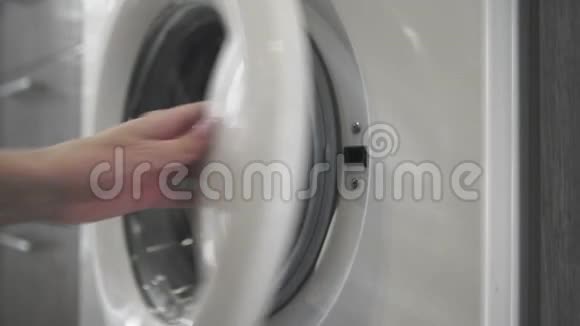 带结婚戒指的女性手把黑色的衣服放进洗衣机里去装洗衣机把衣服装上洗衣机视频的预览图