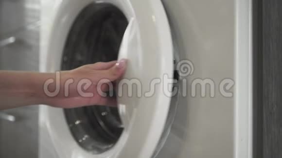 带结婚戒指的女性手把白色的衣服放进洗衣机里去装洗衣机把衣服装上洗衣机视频的预览图
