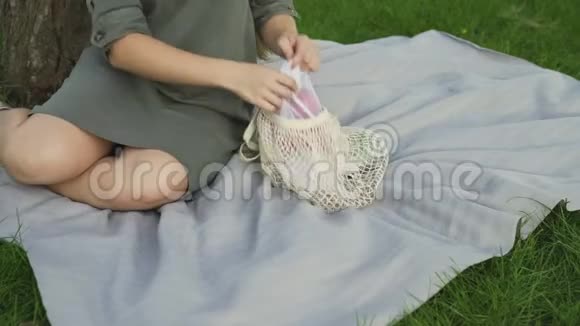 无法辨认的女人坐在毯子上在夏天的公园里从棉网购物袋里拿番茄零废物视频的预览图
