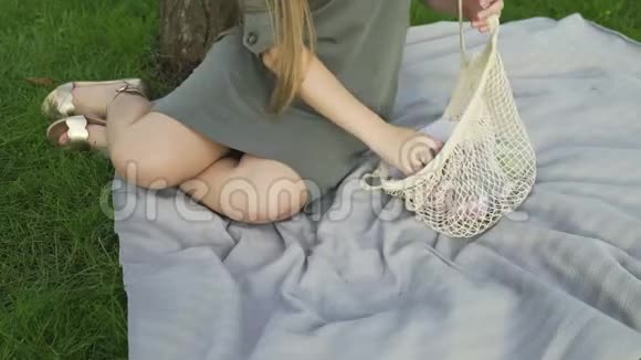 无法辨认的女人坐在毯子上在夏天的公园里从棉网购物袋里拿蔬菜零废物视频的预览图