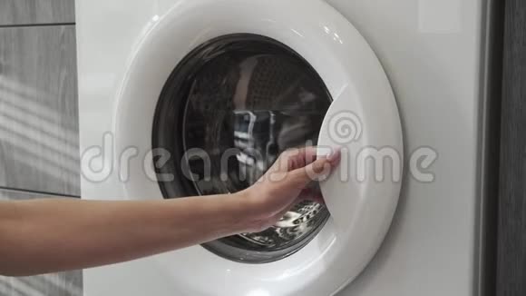 带结婚戒指的女性手在洗衣机里放绿色的衣服去装洗衣机把衣服装上洗衣机视频的预览图