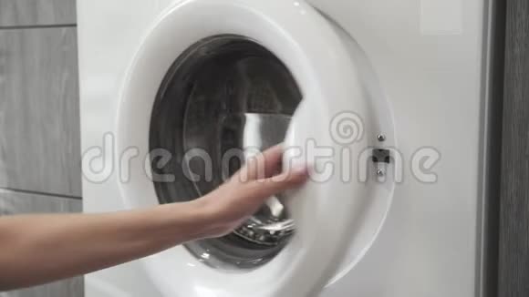 女性手带着结婚戒指把黑色的衣服放在洗衣机里去装洗衣机把衣服装上洗衣机视频的预览图
