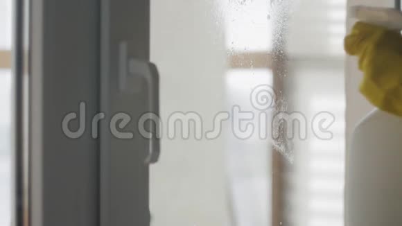 家庭主妇戴黄色手套用白色抹布和洗涤剂清洗窗户视频的预览图