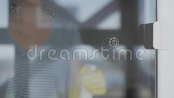 戴黄色手套的年轻女人用白色抹布和洗涤剂洗窗户视频的预览图