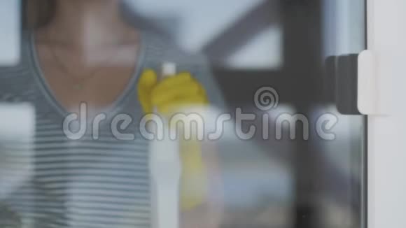 戴黄色手套的年轻女人用黄色抹布和洗涤剂洗窗户视频的预览图