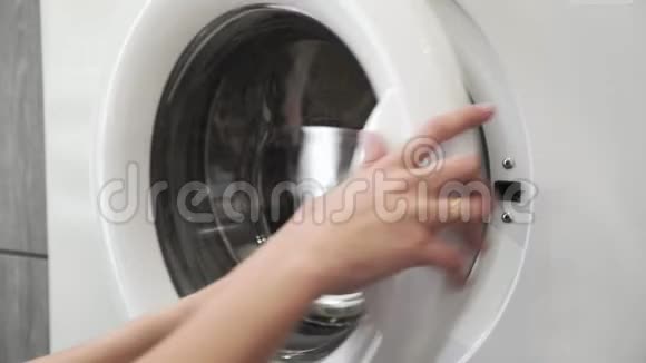 带着结婚戒指的女性手从洗衣机里拿着绿色的SNEAKERS去装洗衣机把衣服装上洗衣机视频的预览图