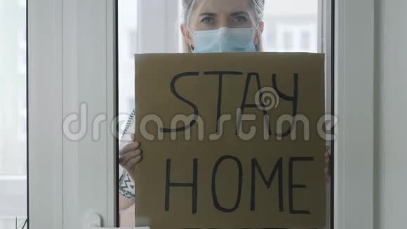 玻璃后面的女人在纸板上留言呆在家里隔离视频的预览图