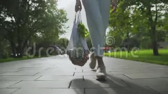 女性的正面景色手里拿着带蔬菜的棉网购物袋在夏季公园散步视频的预览图