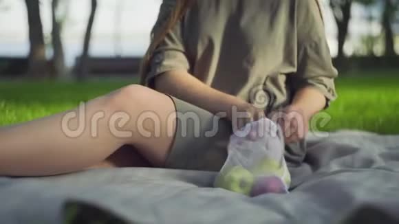 年轻女子坐在毯子上在夏天的公园里从棉网购物袋里拿苹果零浪费购物视频的预览图