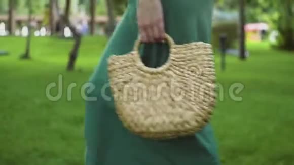 在夏季公园里一个年轻的女人用手工制作的时尚草包走着环保袋视频的预览图