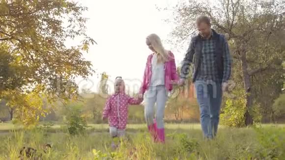 英俊的白种人男人和他的两个女儿在秋天的公园里穿着粉红色的衣服散步幸福家庭视频的预览图