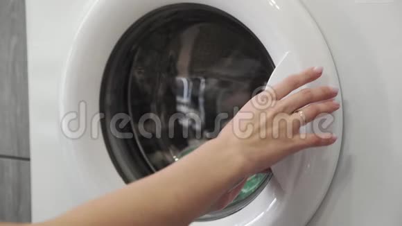带着结婚戒指的女性手从洗衣机里拿着绿色的SNEAKERS去装洗衣机把衣服装上洗衣机视频的预览图
