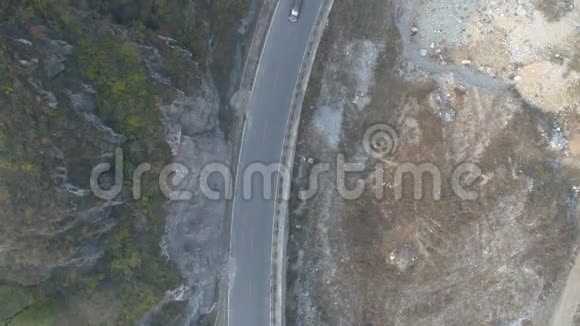 在干燥的山上行驶在一条小沥青路上的白色汽车的鸟瞰图视频的预览图