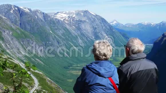 在山上度假的老夫妇成熟的男人和女人享受着绿谷和雪山的景色视频的预览图