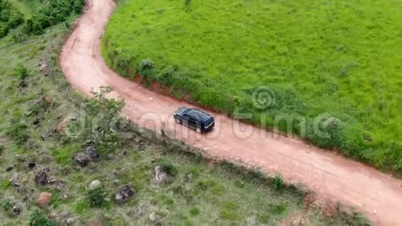 在绿色热带山谷中间的一条小土路上驾驶汽车的鸟瞰图视频的预览图