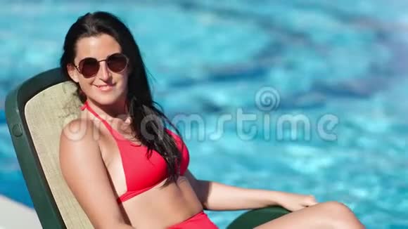 带着时髦太阳镜和泳衣在清澈的蓝水背景下日光浴的微笑旅游女孩视频的预览图