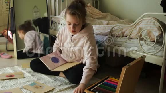 漂亮的女孩坐在房间的地板上用蜡笔画画检疫期快乐少年视频的预览图