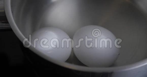 两个生的白鸡蛋在沸水中用不锈钢平底锅煮健康天然蛋白早餐烹饪鸡蛋是视频的预览图