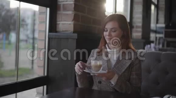 美丽的女人喝咖啡手里拿着一杯卡布奇诺的女孩梦里笑着看着窗外享受着视频的预览图