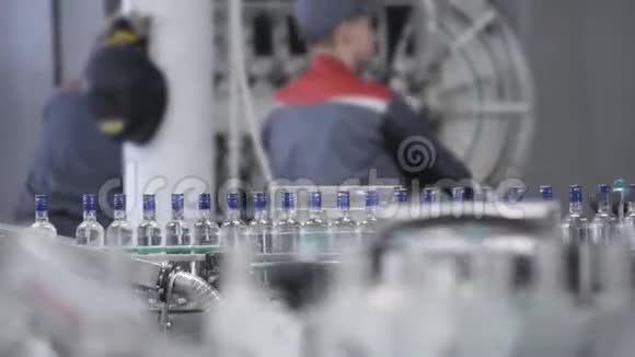 用蓝色箔密封的透明玻璃瓶装酒精沿输送线在工厂装瓶视频的预览图