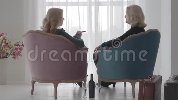 回到成熟的金发白种人女性坐在舒适的扶手椅上交谈高级女性支出视频的预览图