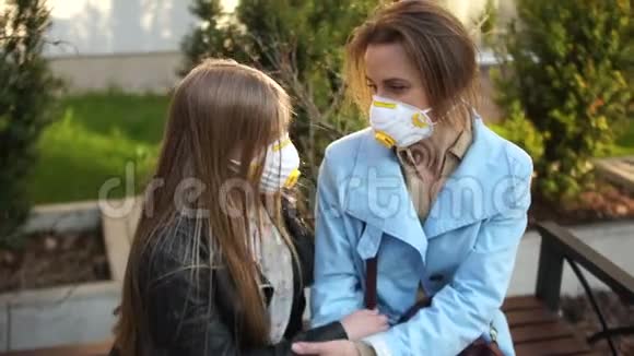 妈妈和女儿一个戴着防护面具的女学生坐在城市公园的长凳上拥抱检疫步行冠状病毒视频的预览图