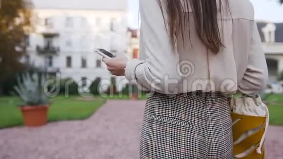 一位留着长发的不可辨认女人的后景她走在漂亮的富有的房子附近使用她的智能手机视频的预览图