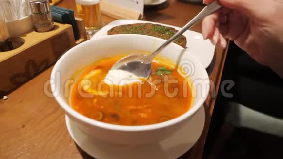 在汤匙上将女性手加入到罗宋汤中加入酸奶油女人在家里的餐桌上搅拌奶油汤大杂烩视频的预览图