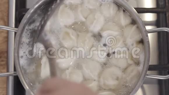 慢镜头顶部的镜头煮饺子在沸水锅男子用平底锅搅拌饺子视频的预览图