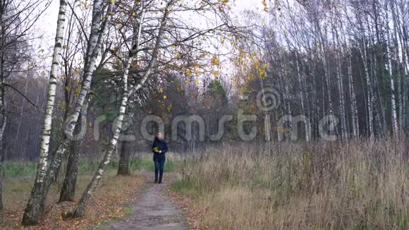 一个穿着蓝色夹克衫手里拿着秋花的苗条美女沿着小路走过秋天公园视频的预览图