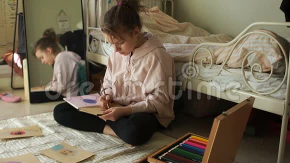 少女坐在房间里的地板上用彩色铅笔在素描盒里画画快乐少年视频的预览图