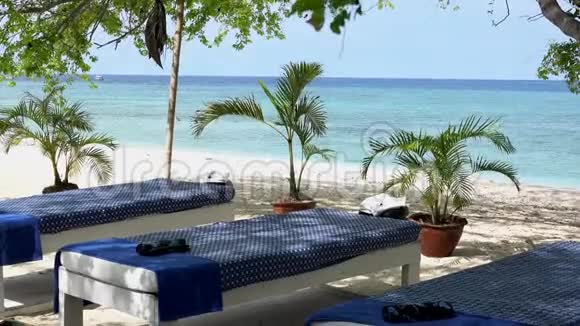 在印度尼西亚吉利岛的一个异国风情的地方沙滩上靠近海边的棕榈树之间的按摩桌和白沙视频的预览图