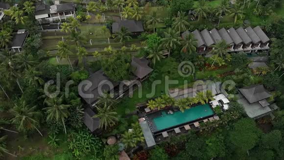 带草屋顶别墅和热带丛林游泳池棕榈树稻田的豪华酒店的高空俯视图视频的预览图