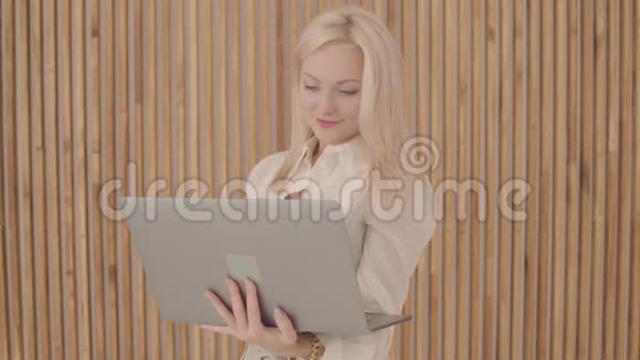 美丽的白人妇女金发和灰色的眼睛拿着笔记本电脑做胜利的手势自信的年轻人视频的预览图