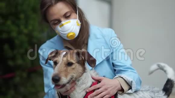 年轻的女人戴着保护面具拥抱她的宠物狗检疫期间冠状病毒流行covid2019宠物护理视频的预览图