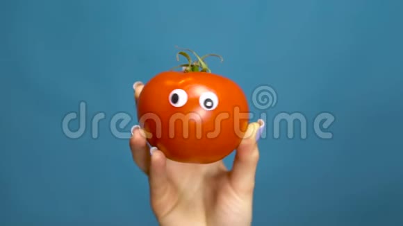 红番茄的眼睛在一个女人的手特写番茄在蓝色背景上摇动和扭曲眼睛慢动作视频的预览图