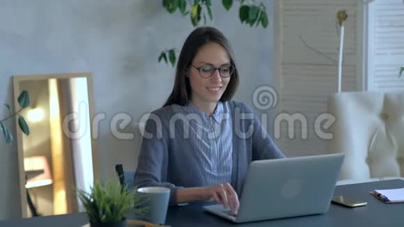 漂亮的女人在笔记本电脑上打字在办公室工作看着相机和微笑视频的预览图