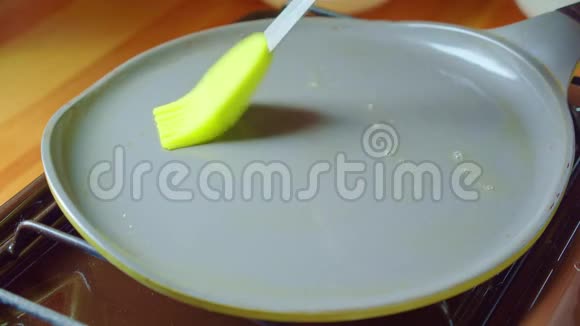 用绿色硅橡胶刷将黄油涂在厨房炉子上的热锅上视频的预览图