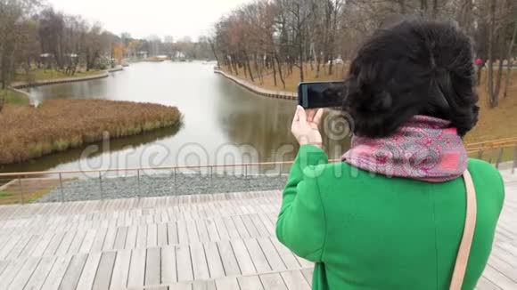 秋天阴天女人在公园里拍池塘的照片从后面看视频的预览图