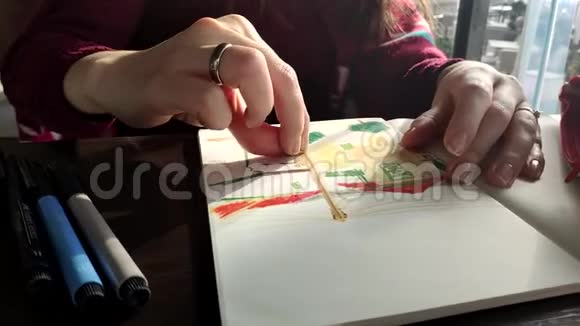 年轻的高加索女艺术家坐在桌上画一幅来自大自然的素描穿着毛衣阳光来自视频的预览图