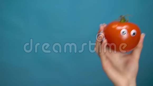 红番茄女人手里拿着眼睛番茄跳进框架在蓝色背景上环顾四周女人的手视频的预览图