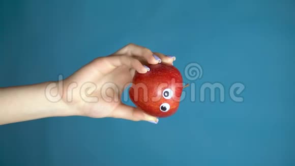 红苹果的眼睛在一个女人的手上闭上苹果在蓝色背景下环顾四周垂直视频视频的预览图