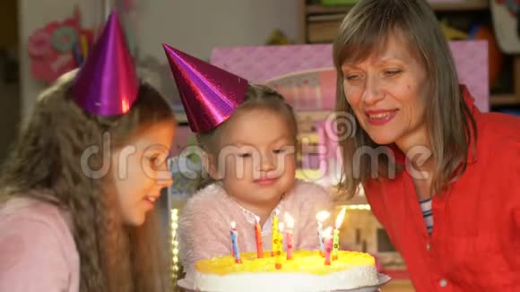 中年妇女和她的孙女戴着派对帽送蛋糕和吹蜡烛视频的预览图