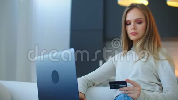 家里有笔记本电脑和信用卡的微笑女人室内有笔记本电脑和银行卡的女孩美丽的女人坐在视频的预览图