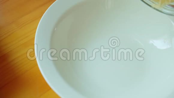 黄色的玉米粉从木桌上的罐子里卷成白色的盘子特写视频的预览图