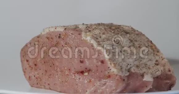 一块新鲜的生猪肉撒上香料塞上大蒜准备在烤箱里烤旋转在白色的pla上视频的预览图