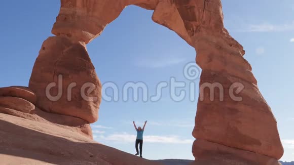 游客举起双手站在国家公园内一座精致的橙色岩石拱门中视频的预览图