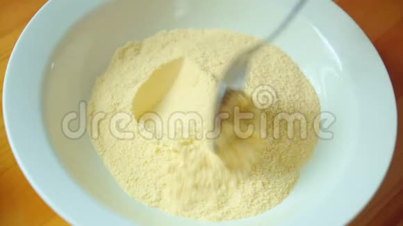 的手用勺子在木桌上用白碗搅动黄色的玉米粉视频的预览图