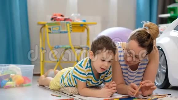 年轻快乐的母亲和小儿子躺在孩子们房间里一起做工艺品画画视频的预览图
